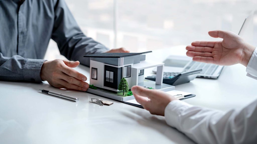 Dos hombres hablan con una maqueta de una casa sobre una mesa